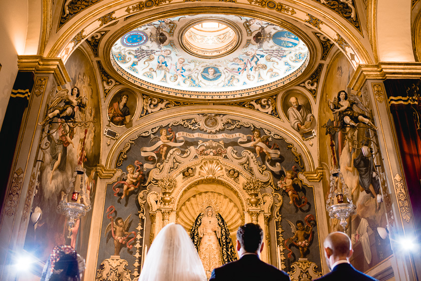 Pareja de recien casados frente al altar de la parroquia de San Roque en su Boda en la Hermandad de los Negritos, fotografía por Moisés García para Bodas con Arte, fotógrafo de bodas en Sevilla Este.